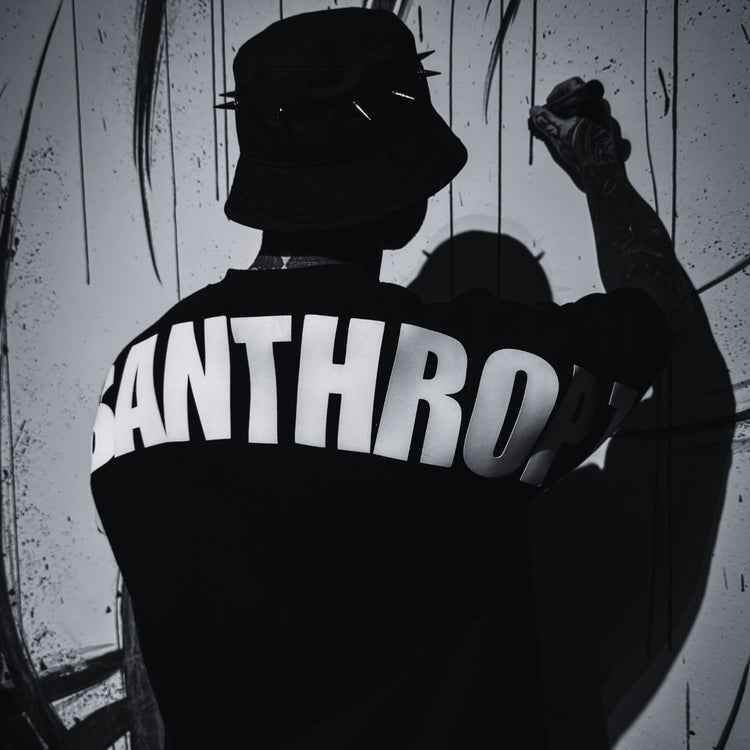 Rückansicht eines Models im MSNTRPZ® MISANTHROPZ® Premium-Shirt mit großem Backprint, während es vor einer bemalten Wand arbeitet; düstere Noir-Streetwear-Ästhetik | Premium German Streetwear