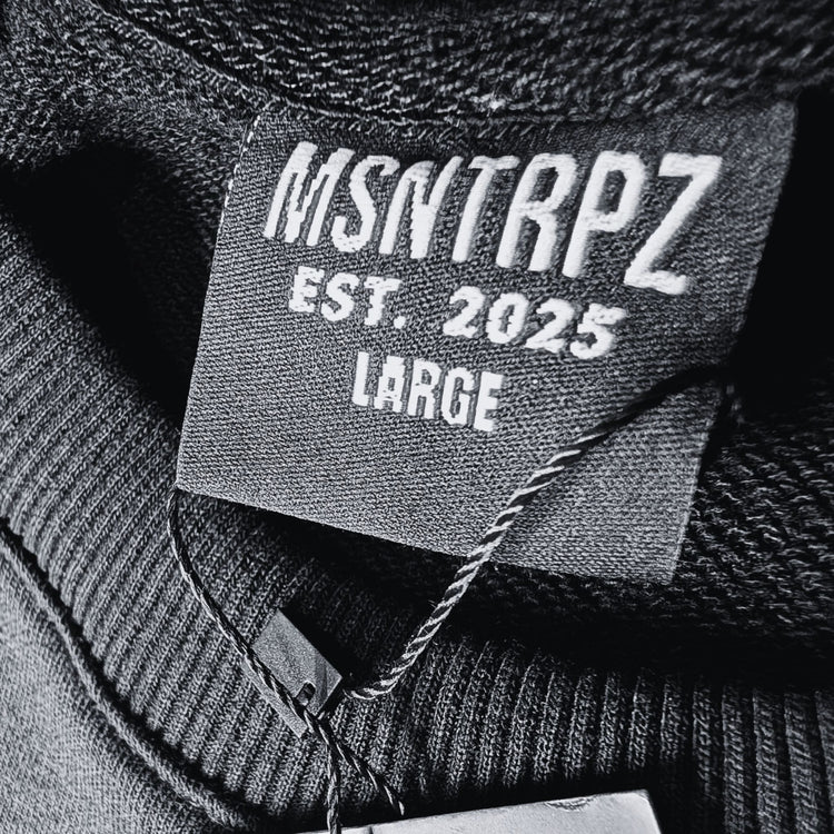 Nahaufnahme des gewebten Halslabels „MSNTRPZ® EST. 2025“ in Größe Large; Premium Noir Streetwear für Unisex