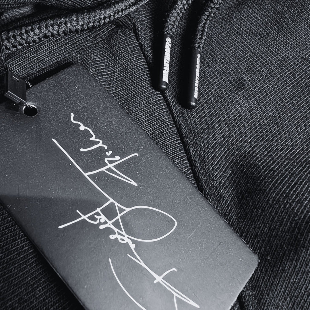 Nahaufnahme eines schwarzen MSNTRPZ® Hoodies mit signiertem Hangtag und gebrandeten Kordelenden; Premium German Streetwear im Noir-Stil