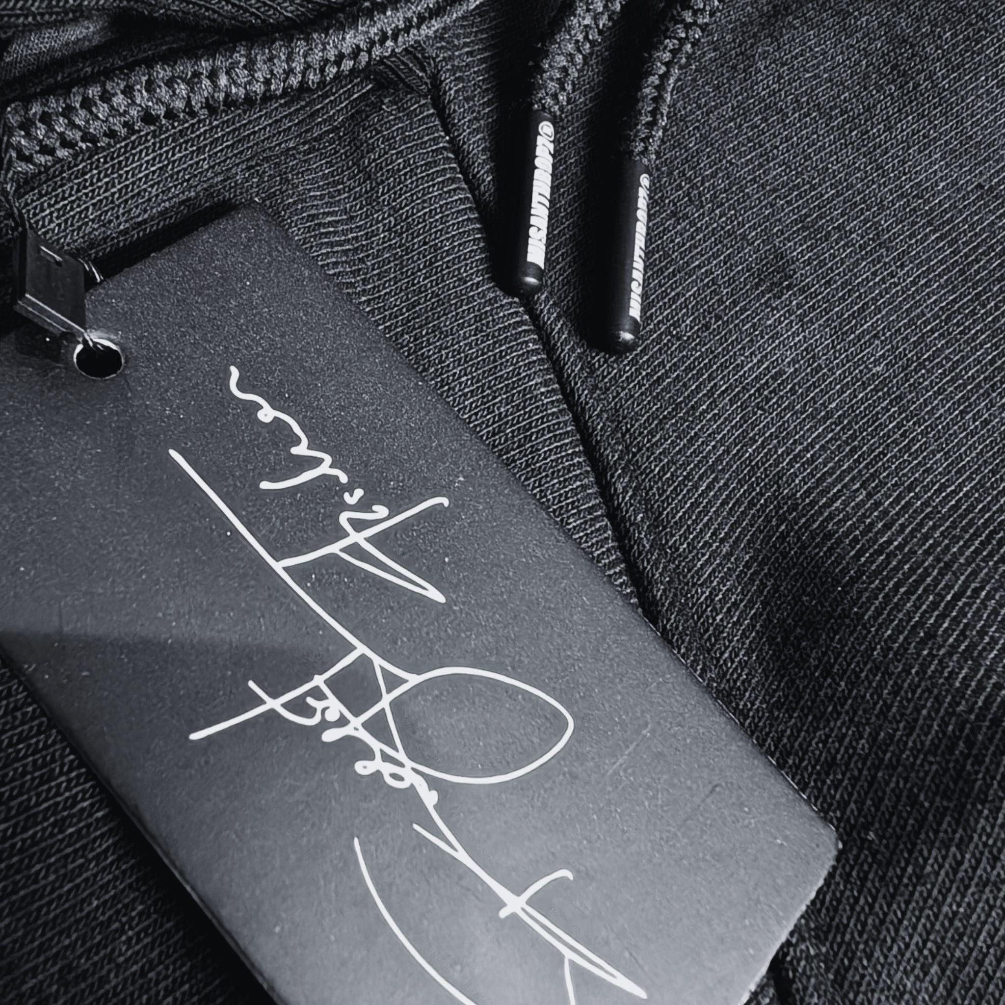 Nahaufnahme eines schwarzen MSNTRPZ® Hoodies mit signiertem Hangtag und gebrandeten Kordelenden; Premium German Streetwear im Noir-Stil