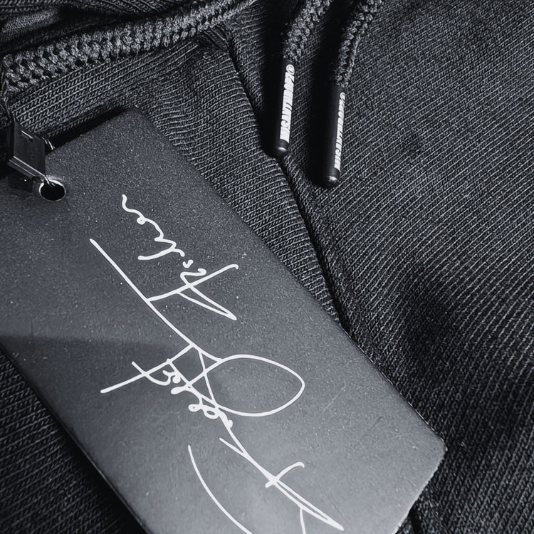 Nahaufnahme eines schwarzen MSNTRPZ® Hoodies mit signiertem Hangtag und gebrandeten Kordelenden; Premium German Streetwear im Noir-Stil