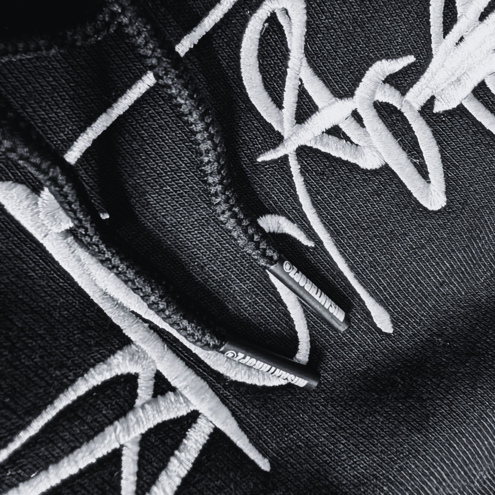 Detailaufnahme des MSNTRPZ® MISANTHROPZ® Hoodies mit gesticktem Signature-Schriftzug und markenprägten Kordelenden; hochwertige Textur im Noir-Stil | Premium German Streetwear
