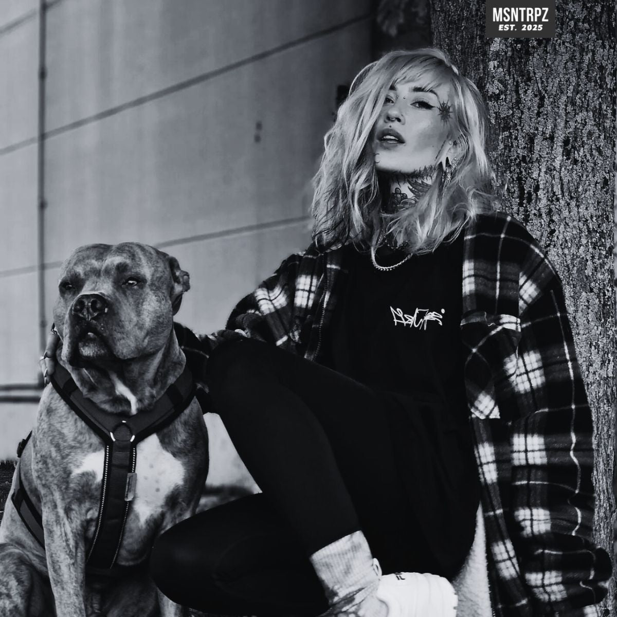 MSNTRPZ® MISANTHROPZ® Noir-Portrait eines tätowierten weiblichen Models im Premium-Streetwear-Shirt neben einem kräftigen Hund. Die ruhige, authentische Szene unterstreicht die Outsider-Mentalität der Misanthropz® Community – echte Souls, echte Loyalität, Premium German Streetwear.