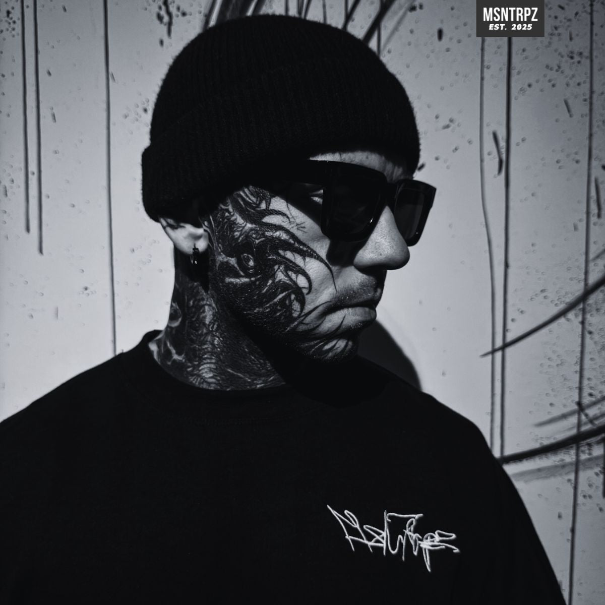 MSNTRPZ® MISANTHROPZ® Noir-Portrait eines stark tätowierten Models mit Beanie und Sonnenbrille im schwarzen Premium Streetwear-Shirt | Premium German Streetwear