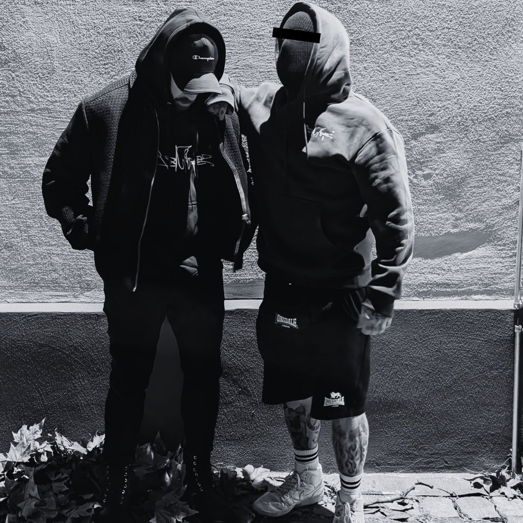 MSNTRPZ® MISANTHROPZ® Noir-Portrait zweier vermummter Models in schwarzer Oversize Streetwear mit Hoodie und Cap | Premium German Streetwear