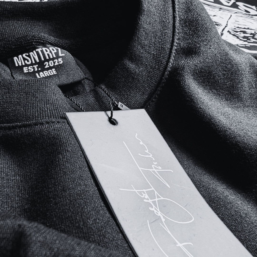 Nahaufnahme eines schwarzen MSNTRPZ® Shirts mit gewebtem Halslabel „EST. 2025“ und signiertem Hangtag; Premium Noir Streetwear für Unisex