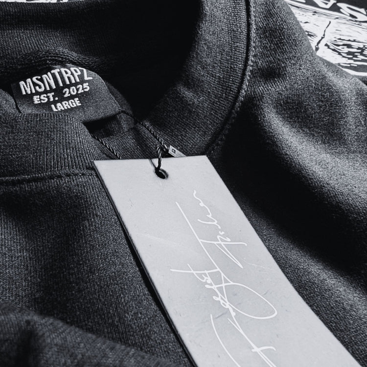 Nahaufnahme eines schwarzen MSNTRPZ® Shirts mit gewebtem Halslabel „EST. 2025“ und signiertem Hangtag; Premium Noir Streetwear für Unisex