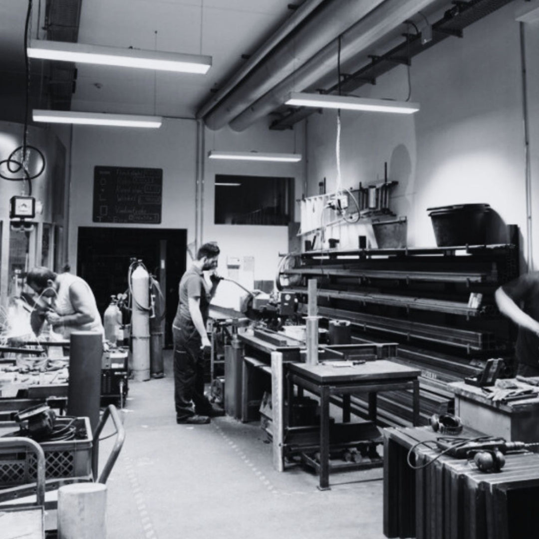 MSNTRPZ® MISANTHROPZ® Aufnahme einer Werkstatt mit mehreren arbeitenden Personen, die handwerkliche Produktionsschritte ausführen; industrielles Noir-Setting | Premium German Streetwear