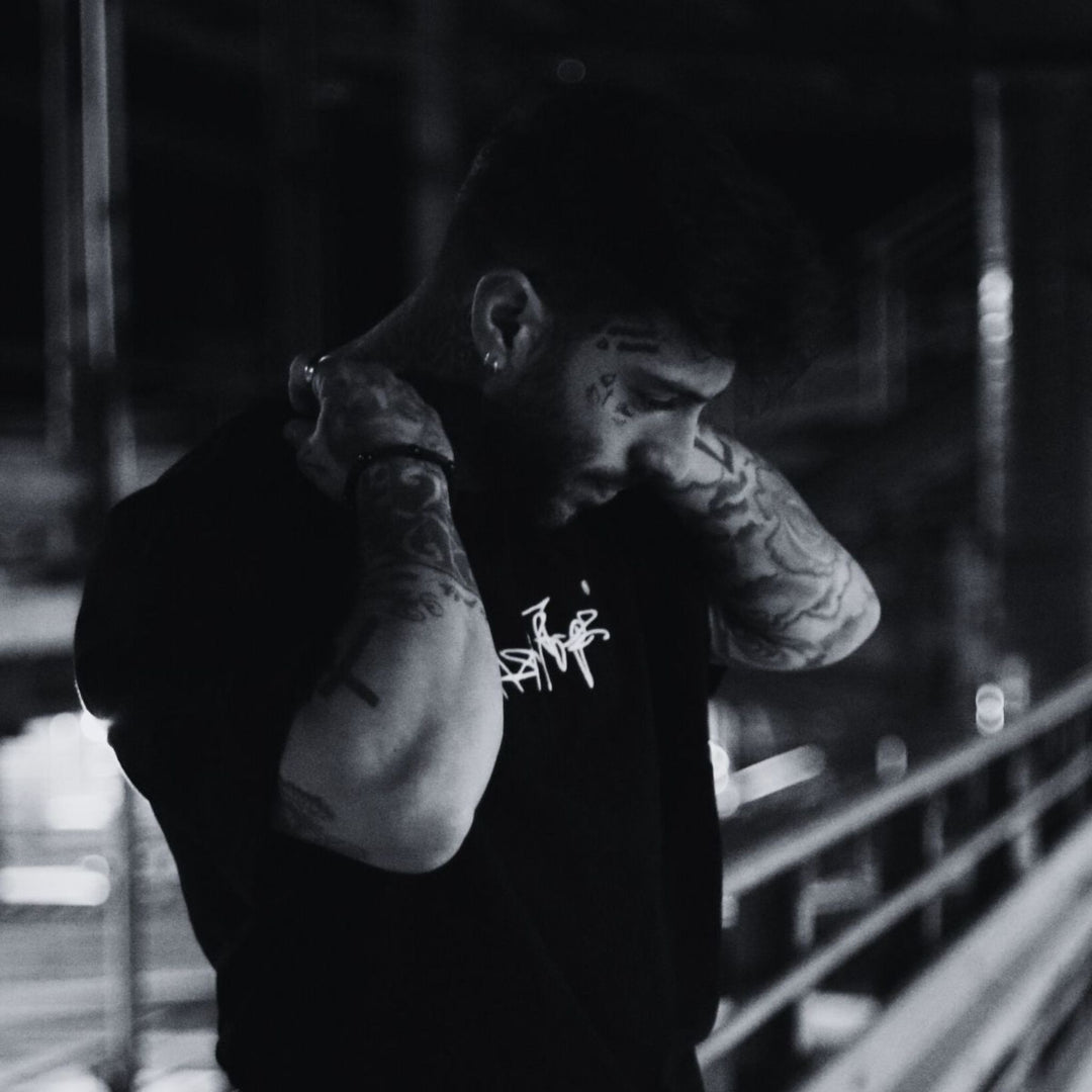 MSNTRPZ® MISANTHROPZ® Nachtaufnahme eines tätowierten Models im schwarzen Premium-Streetwear-Shirt, im charakteristischen Noir-Look der Premium German Streetwear-Kollektion.