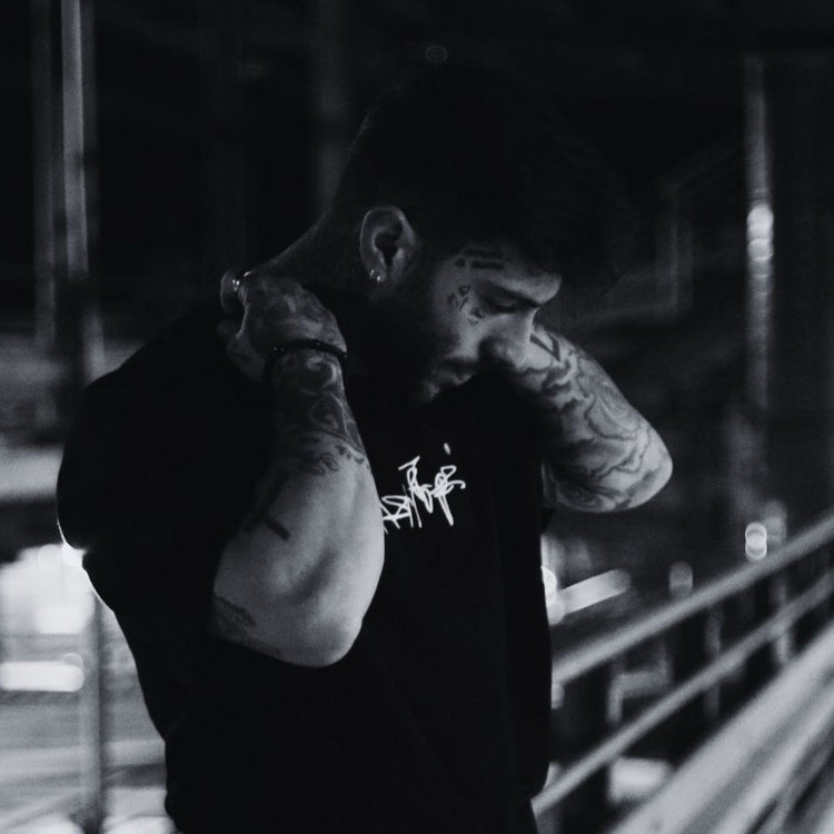 MSNTRPZ® MISANTHROPZ® Nachtaufnahme eines tätowierten Models im schwarzen Premium-Streetwear-Shirt, im charakteristischen Noir-Look der Premium German Streetwear-Kollektion.