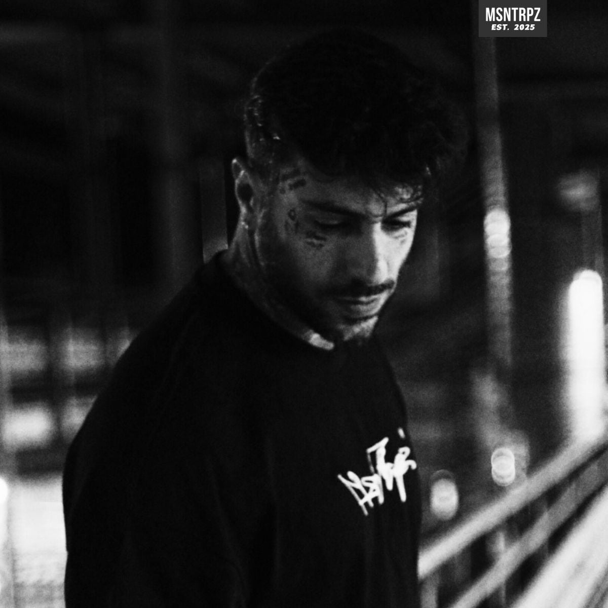 MSNTRPZ® MISANTHROPZ® Noir-Nachtaufnahme eines tätowierten männlichen Models im schwarzen Streetwear-Outfit auf einem Parkdeck – Premium German Streetwear in rauer, atmosphärischer Urban-Ästhetik.