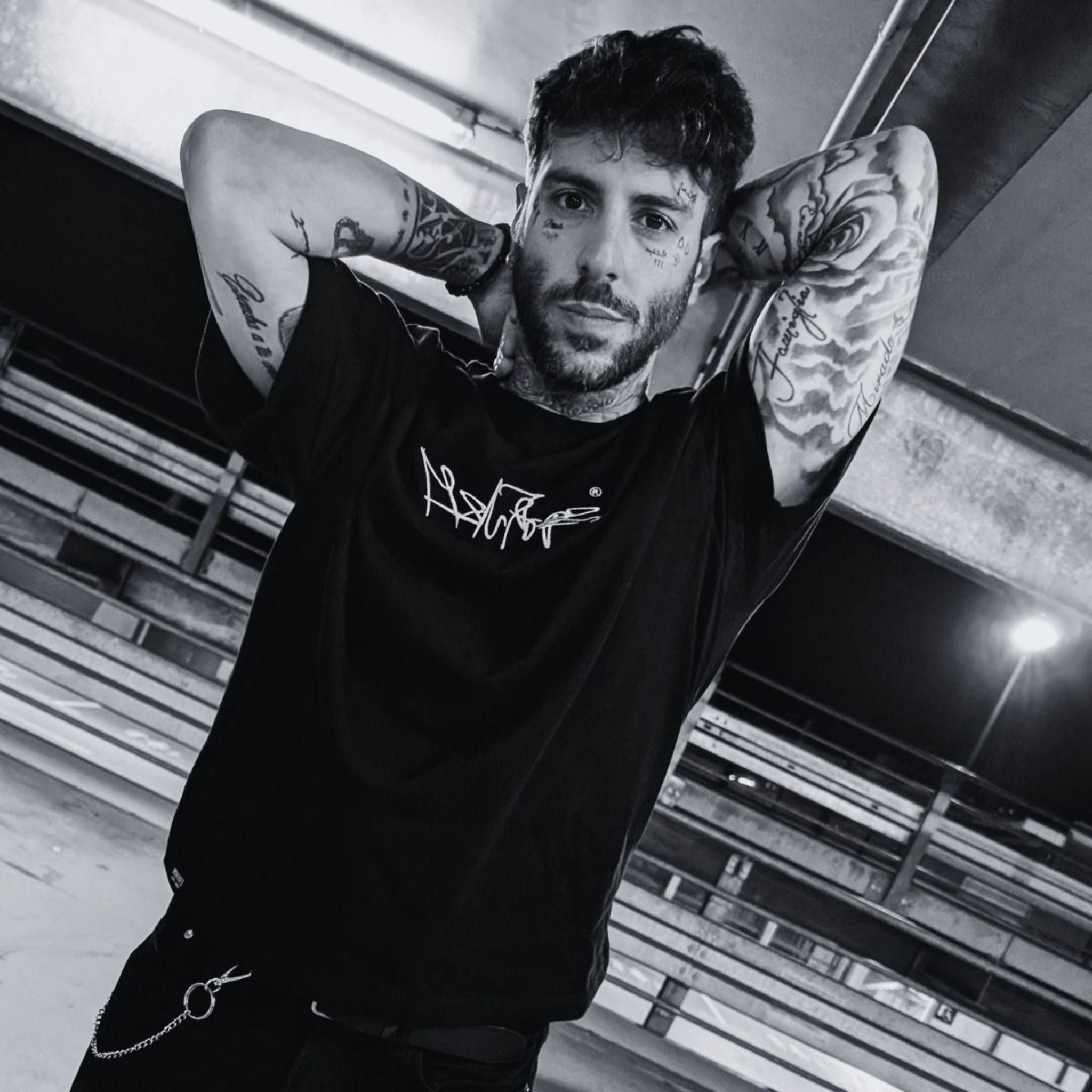 MSNTRPZ® MISANTHROPZ® Noir-Portrait eines tätowierten Models im schwarzen Premium-Streetwear-Shirt, aufgenommen im Parkhaus-Licht – Premium German Streetwear.